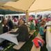 Viele Menschen sitzen auf Bierzeltgarnituren unter Pavillons und unterhalten sich.