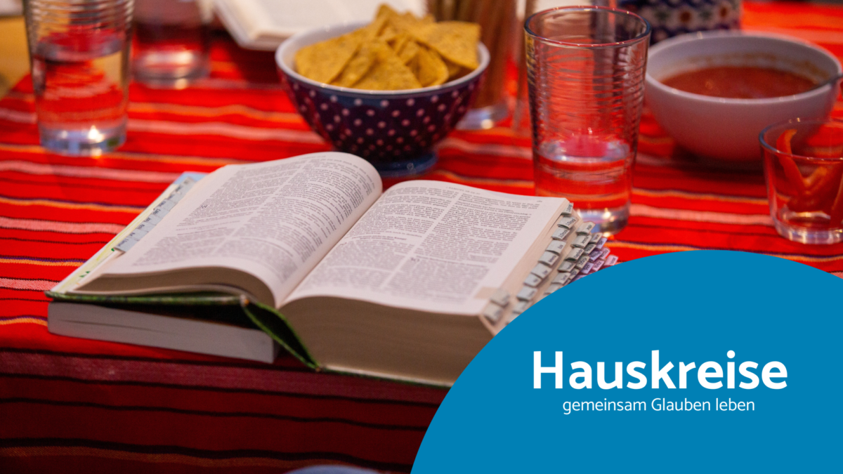 Auf einem Tisch mit einer roten Tischdecke stehen Wassergläser und Snacks. Im Vordergrund liegt eine aufgeschlagene Bibel.