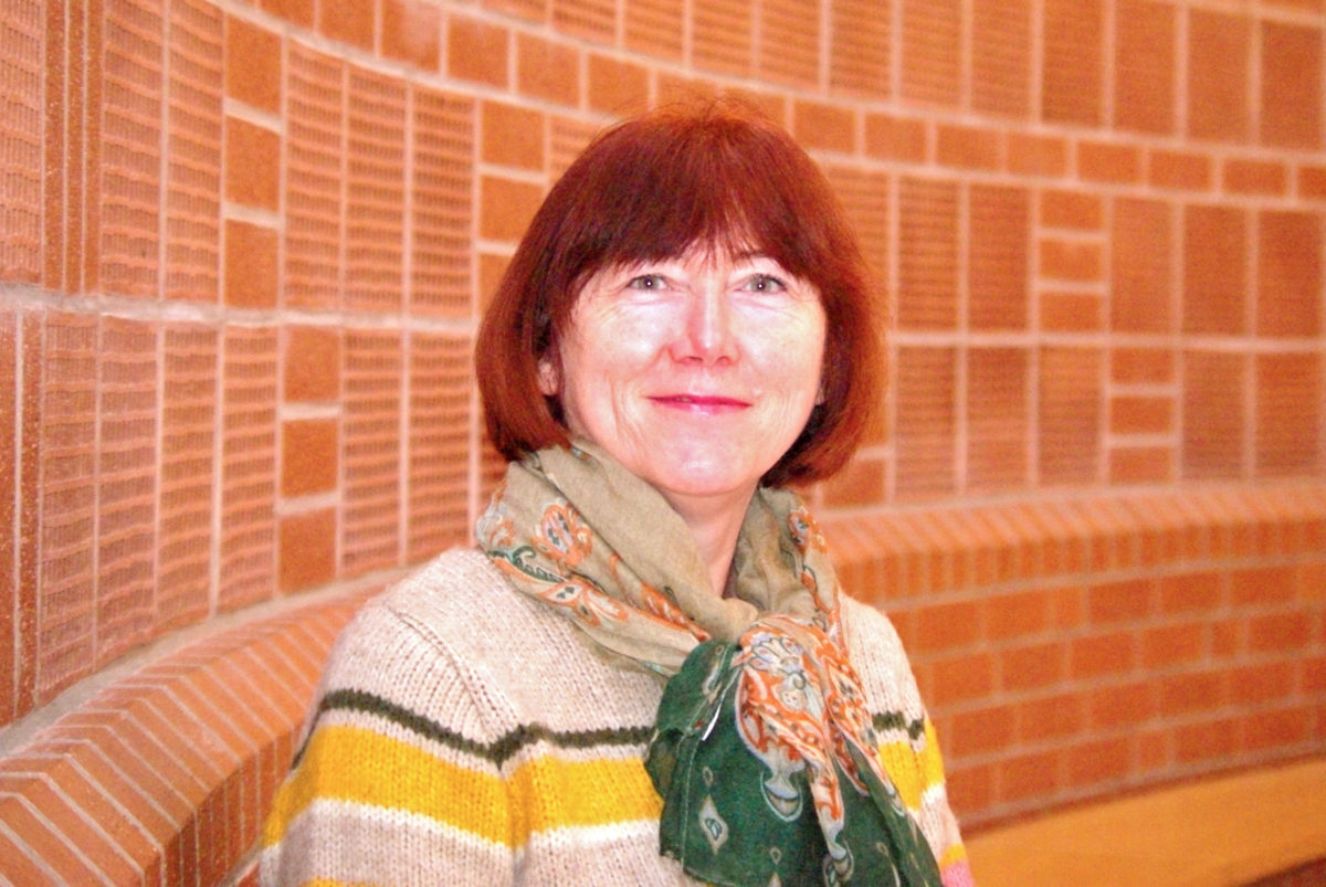 Lilia Fischer, eine Frau mit roten Haaren, sitzt vor einer roten Backsteinmauer in der Elia-Kirche.