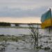 Eine angerissene orange-blaue Flagge der Ukraine steht in einer Moorlandschaft