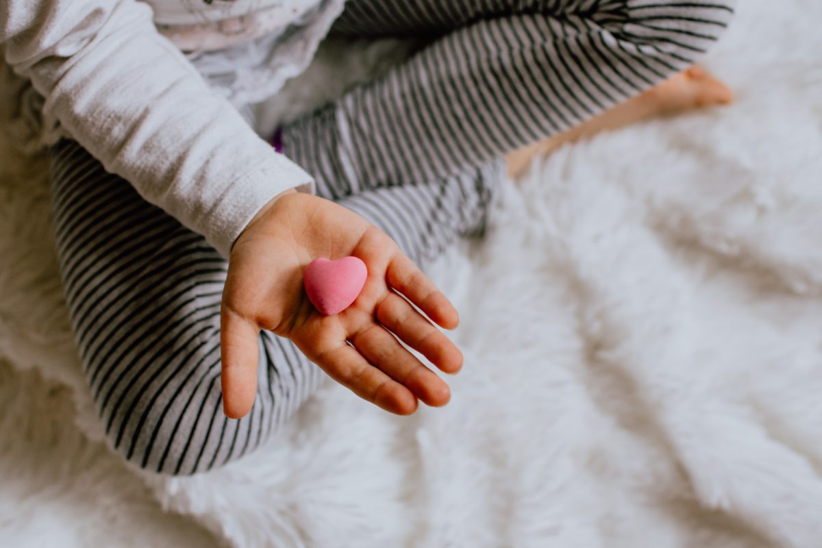 Eine Kinderhand hält ein kleines, rosafarbenes Herz.