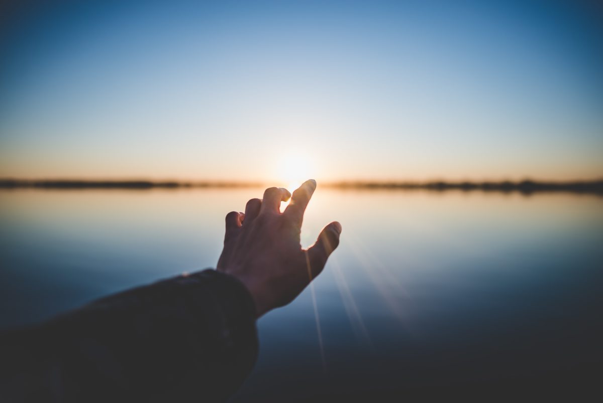 Eine Hand streckt sich dem Sonnenaufgang entgegen