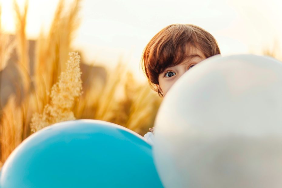 Ein Kind schaut mit großen Augen hinter Lufballons hervor.